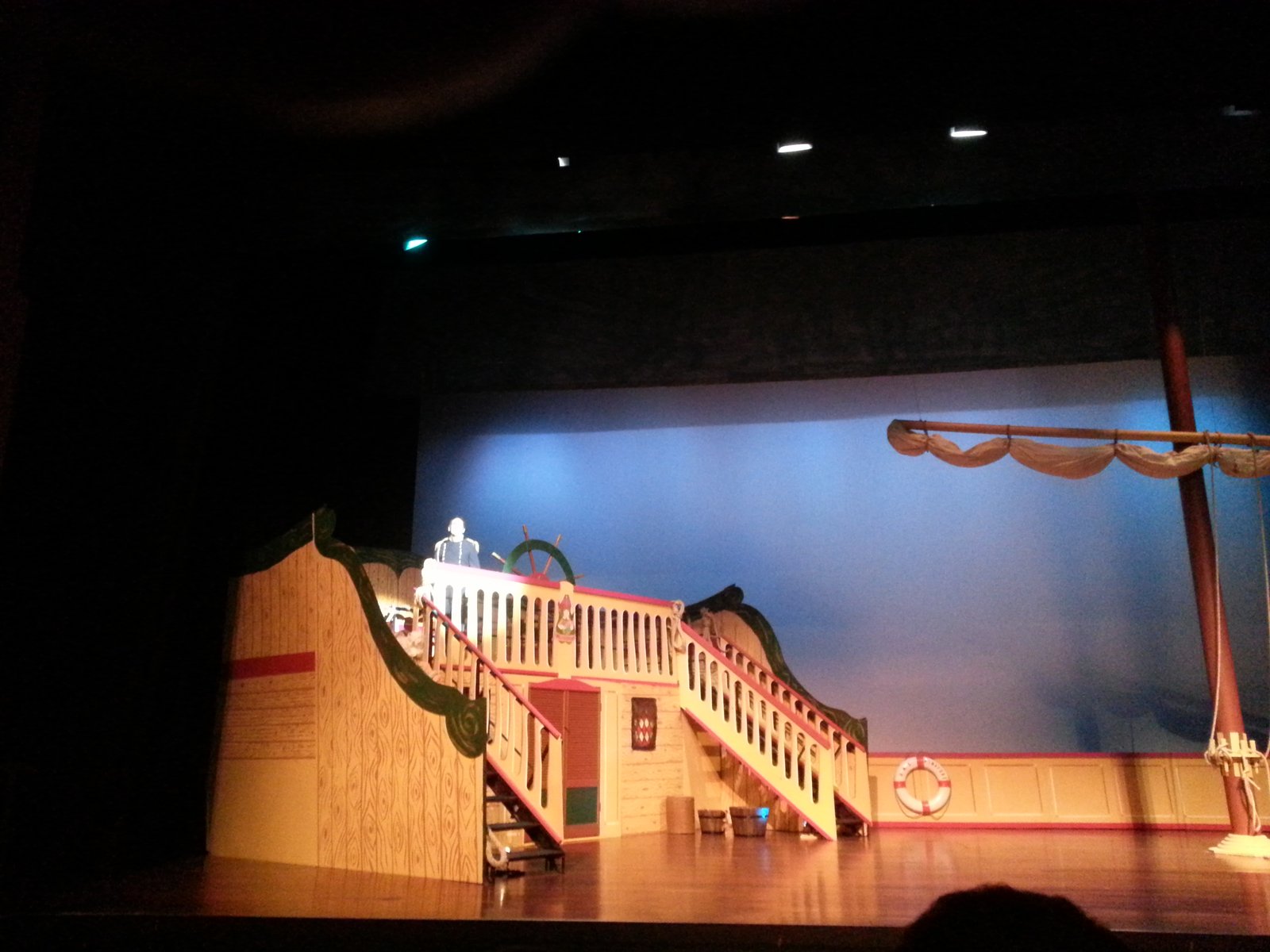 HMS Pinafore stage set in use during a live performance, with an actor at the ship's wheel