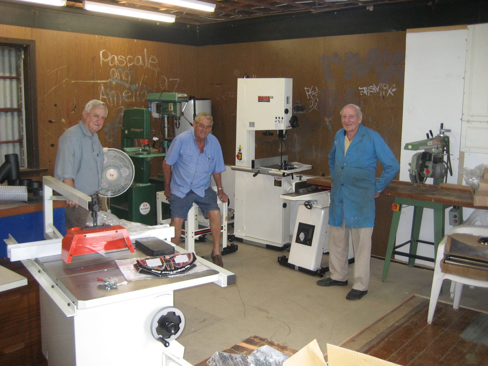 Three Shed members standing with newly arrived workshop machinery inside the still-derelict Howson Oval building