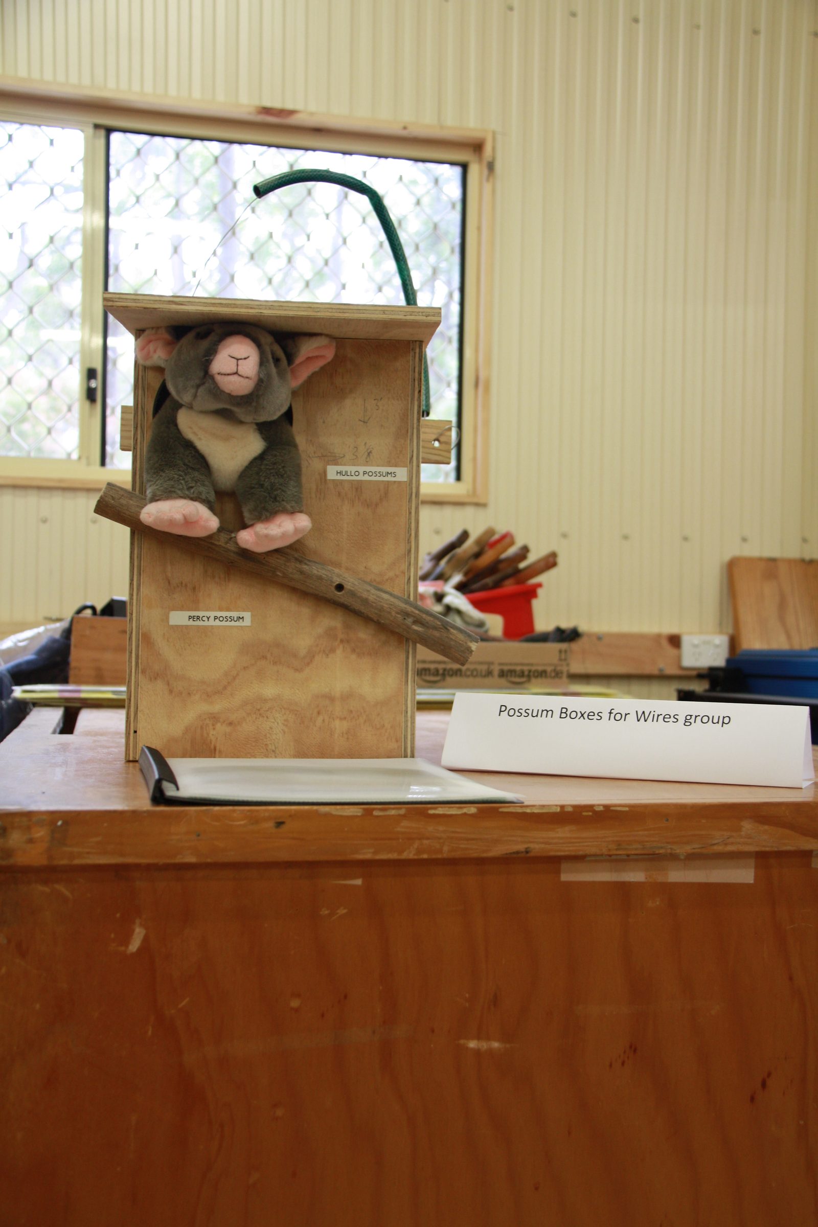 Soft toy possum demonstrating a WIRES nesting box built by Shed members